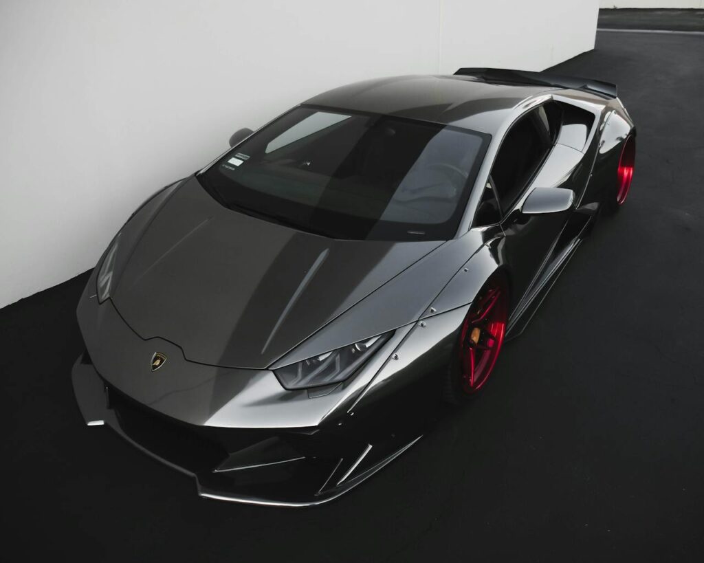 Sleek metallic Lamborghini sports car with vibrant red wheels parked indoors.